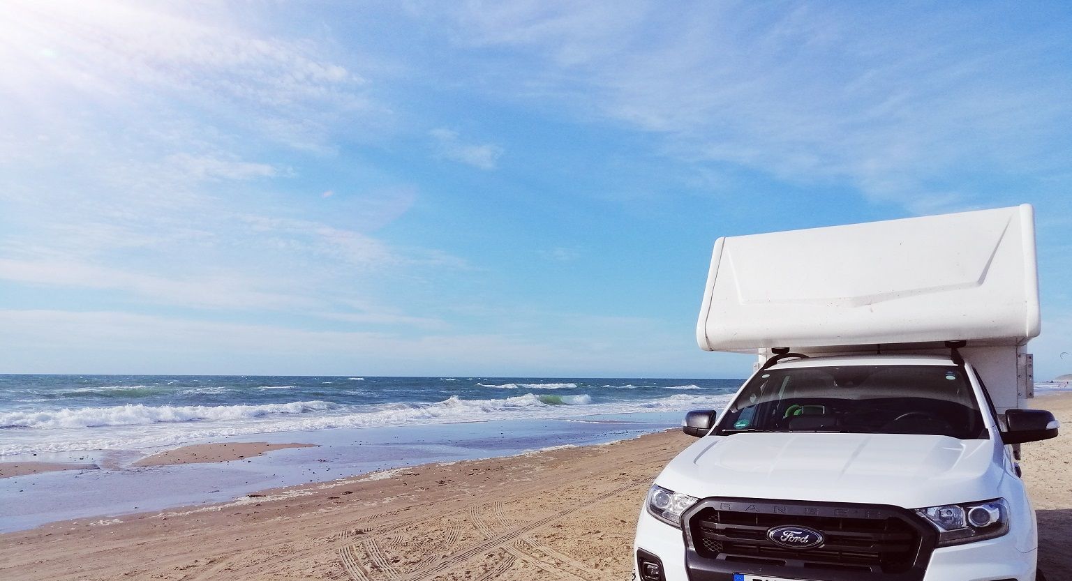 Ein weißer Lastwagen steht am Strand neben dem Meer.
