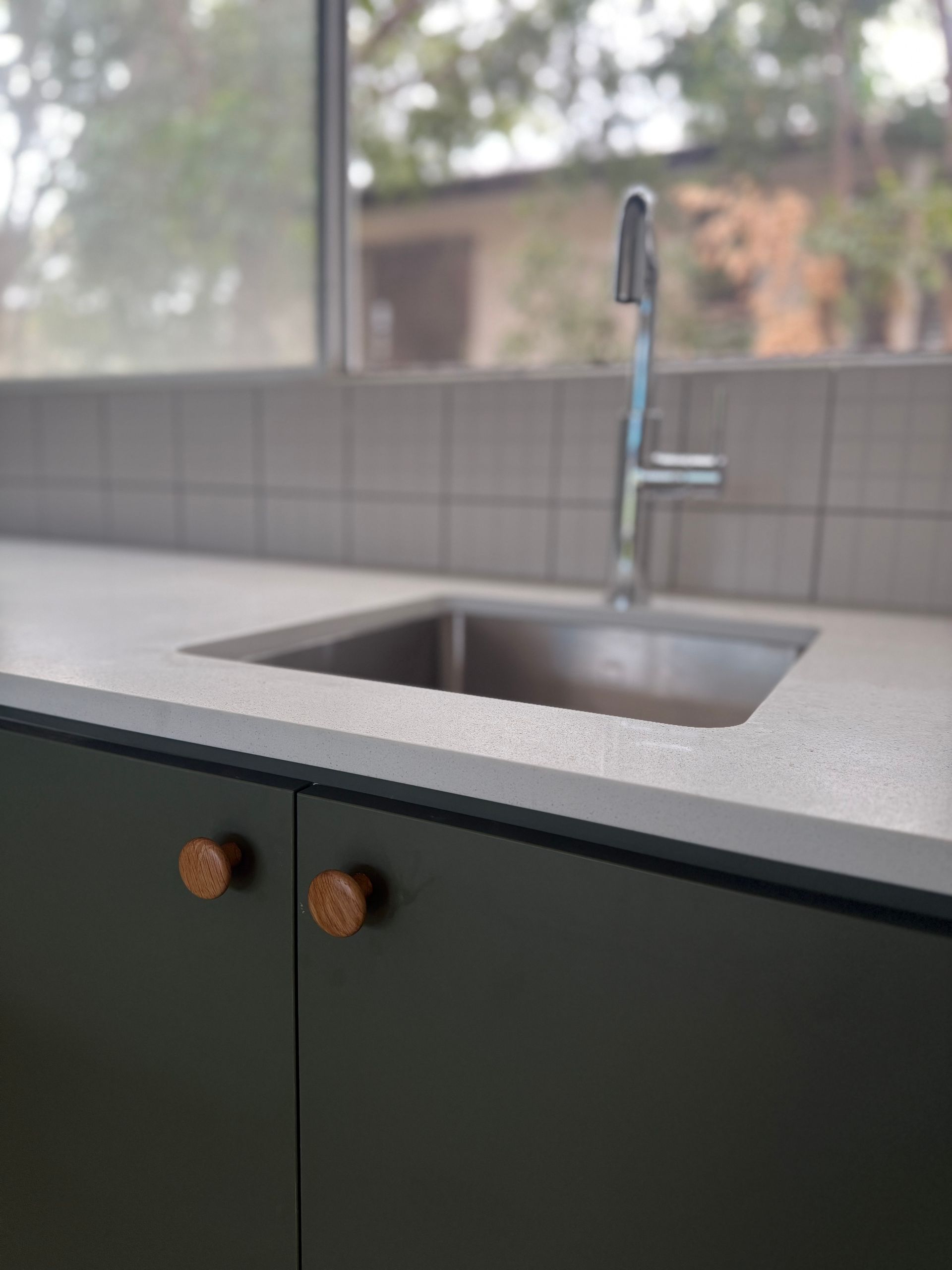 Kitchen sink with green cabinets, copper knobs, and a window view of a building and trees — Canelo Cabinetry In Rocklea, QLD