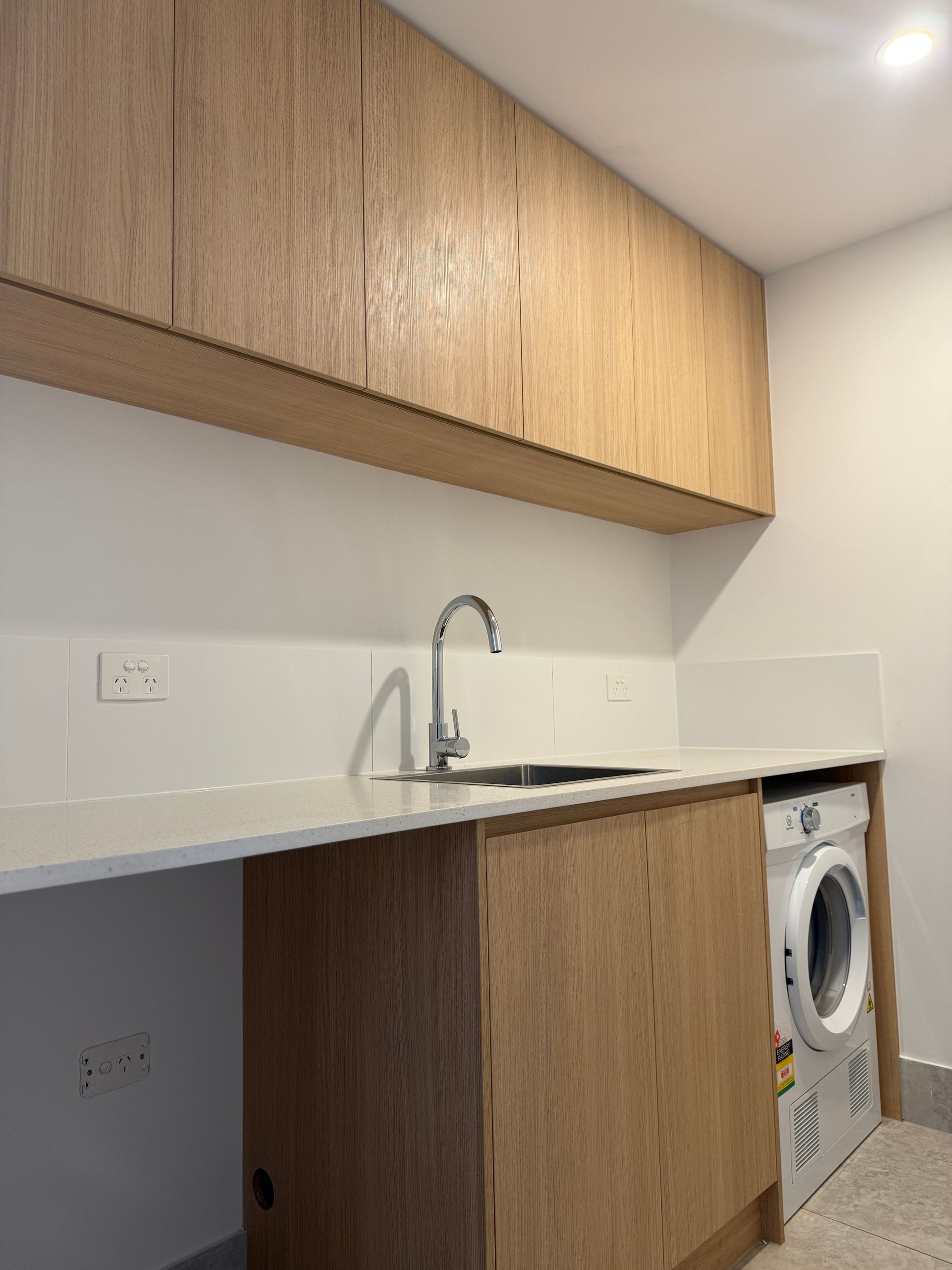 Laundry room with wooden cabinets, white countertop, sink, and washing machine — Canelo Cabinetry In Rocklea, QLD