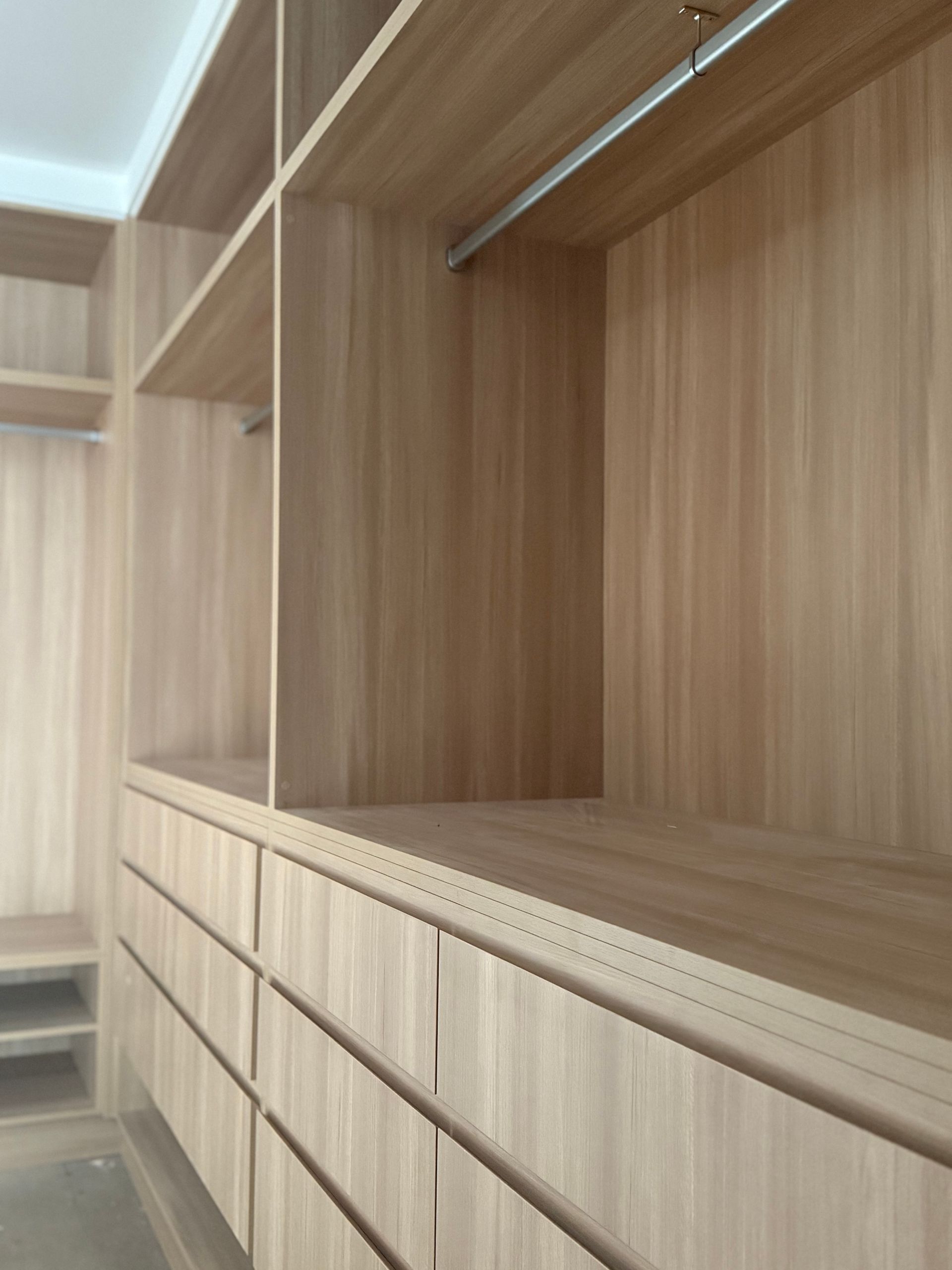 Built-in wooden closet with drawers, shelves, and hanging rods. Neutral wood tones dominate the space — Canelo Cabinetry In Rocklea, QLD