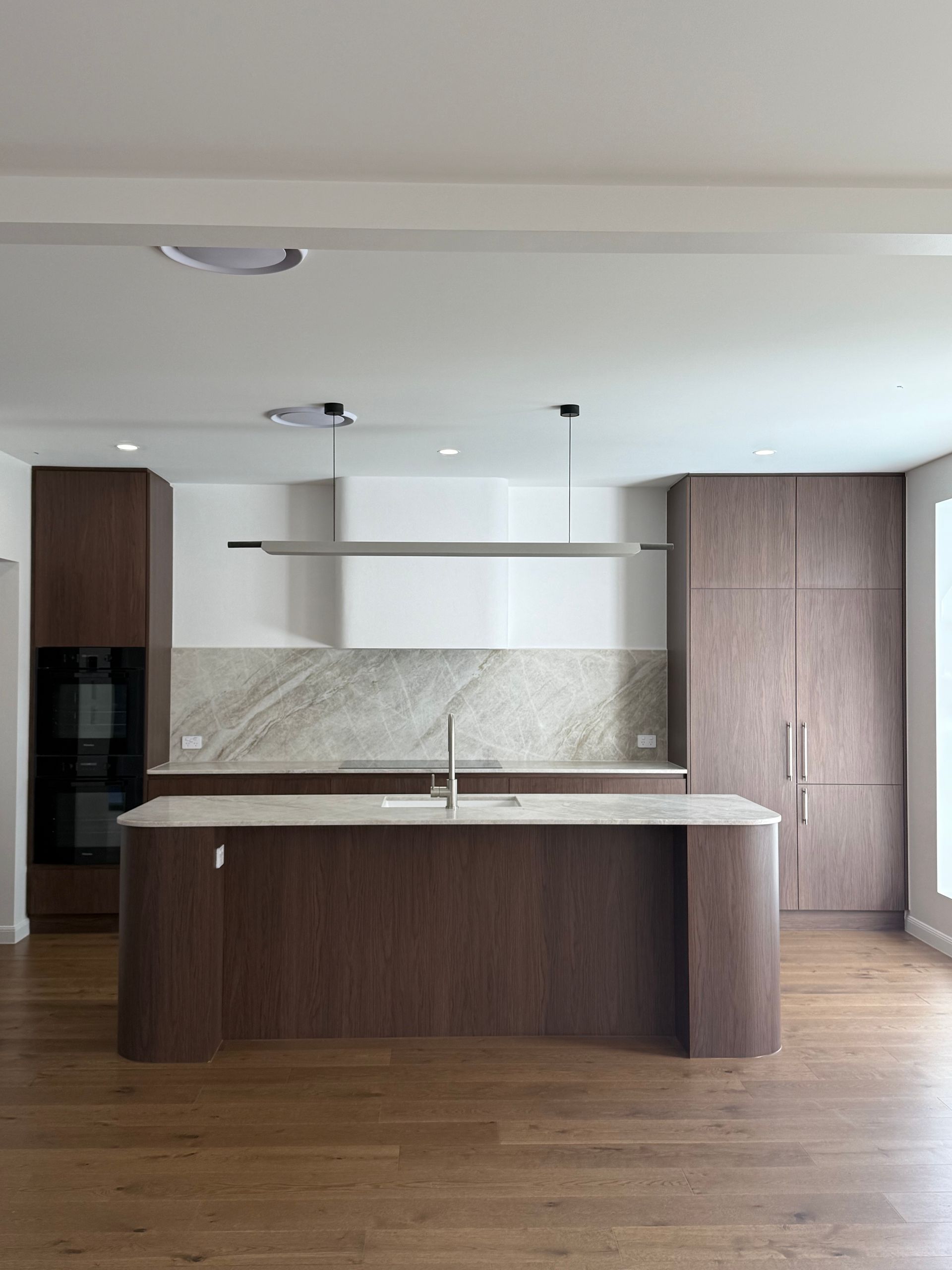 Modern kitchen with wood cabinetry, marble backsplash, and island, light fixtures and wood flooring — Canelo Cabinetry In Rocklea, QLD