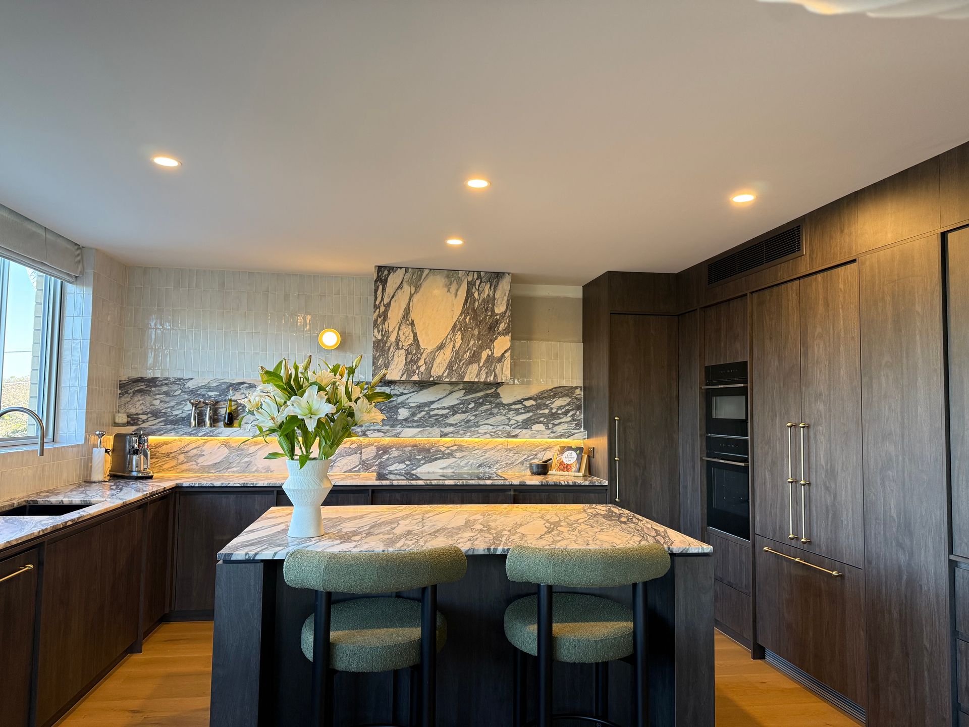 Modern kitchen with marble countertops, wood cabinets, and two green stools at the island — Canelo Cabinetry In Rocklea, QLD