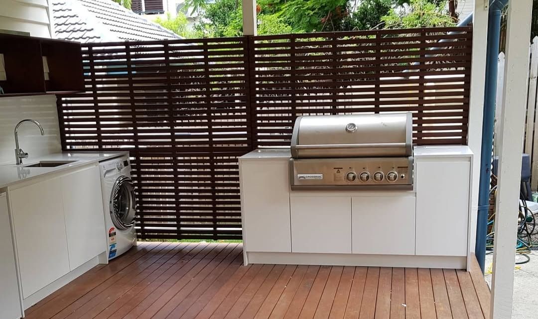 Outdoor Kitchen With Brown Slatted Fence, White Cabinets, Grill, and a Washing Machine — Canelo Cabinetry In Rocklea, QLD