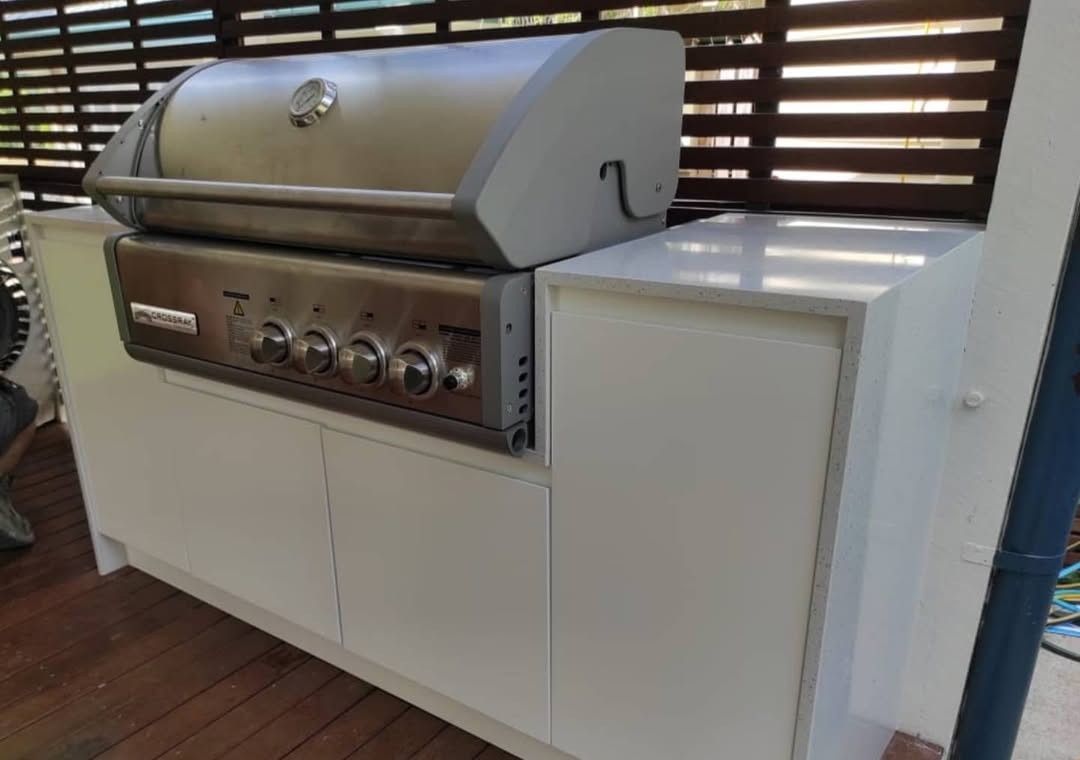White Outdoor Grill Built Into White Cabinets, on a Deck With a Wooden Slat Background — Canelo Cabinetry In Rocklea, QLD