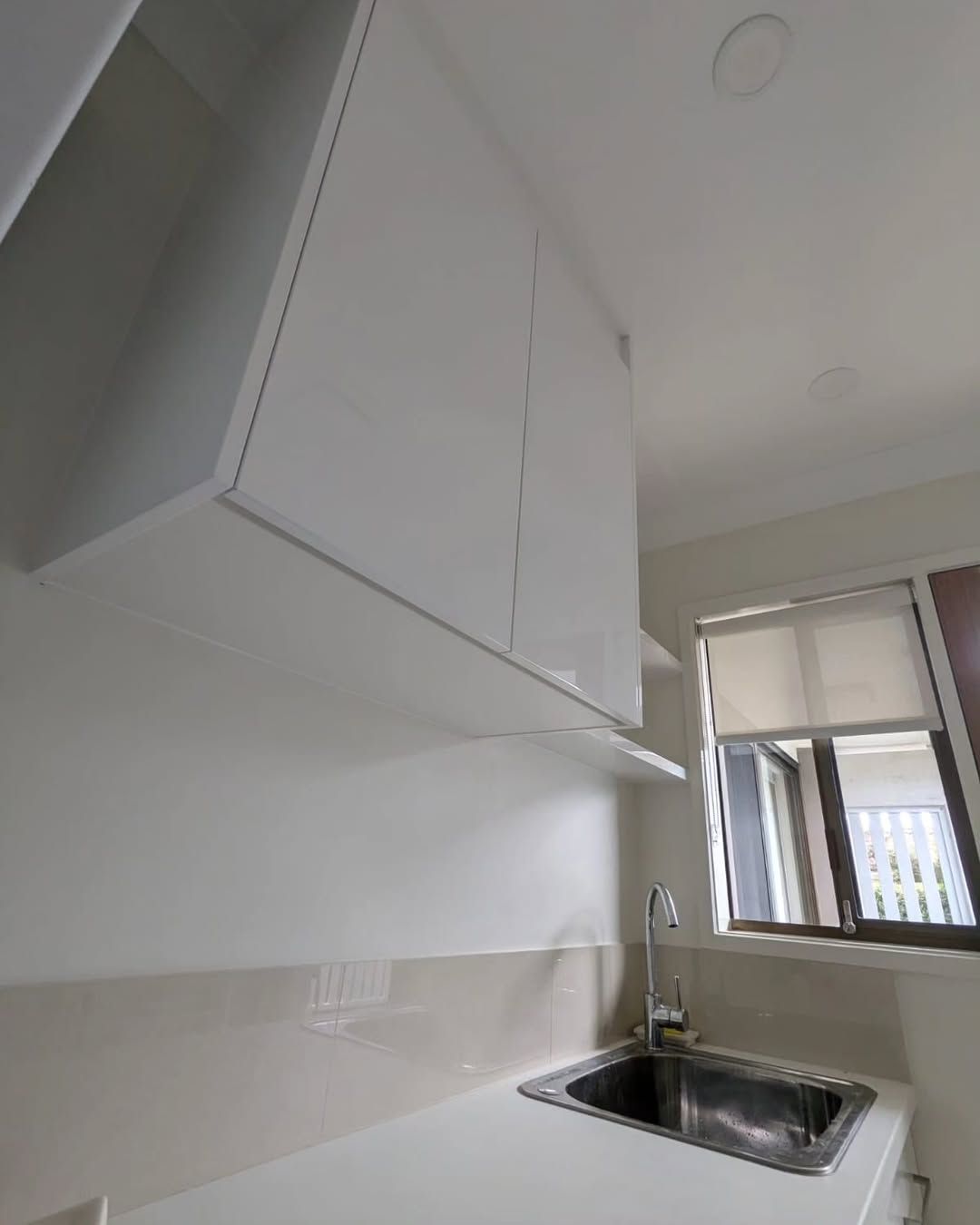 White Kitchen Cabinets Above a Sink, With a Window and Countertop Visible — Canelo Cabinetry In Rocklea, QLD