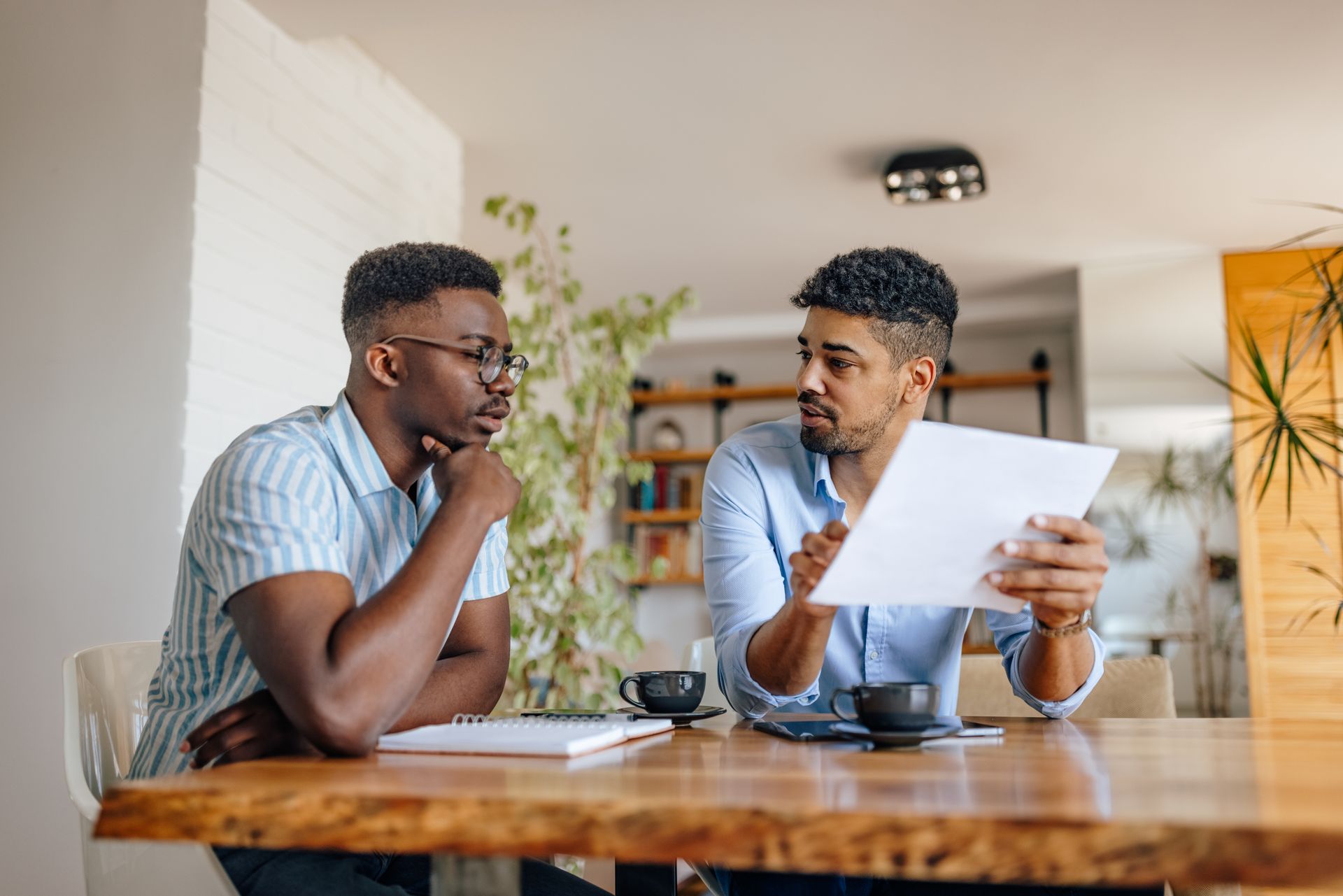 Two men reviewing documents at a table. One points while speaking; the other looks on thoughtfully.