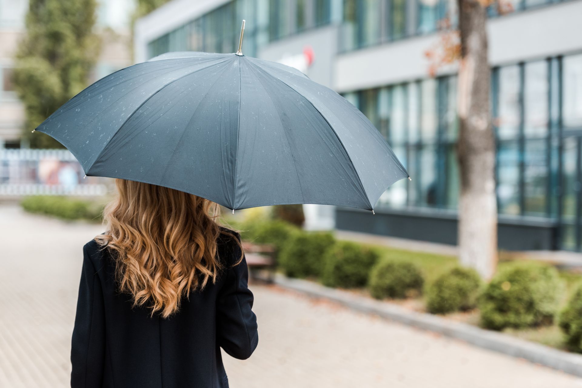 Woman walking under a black umbrella on a rainy day in front of a building.
