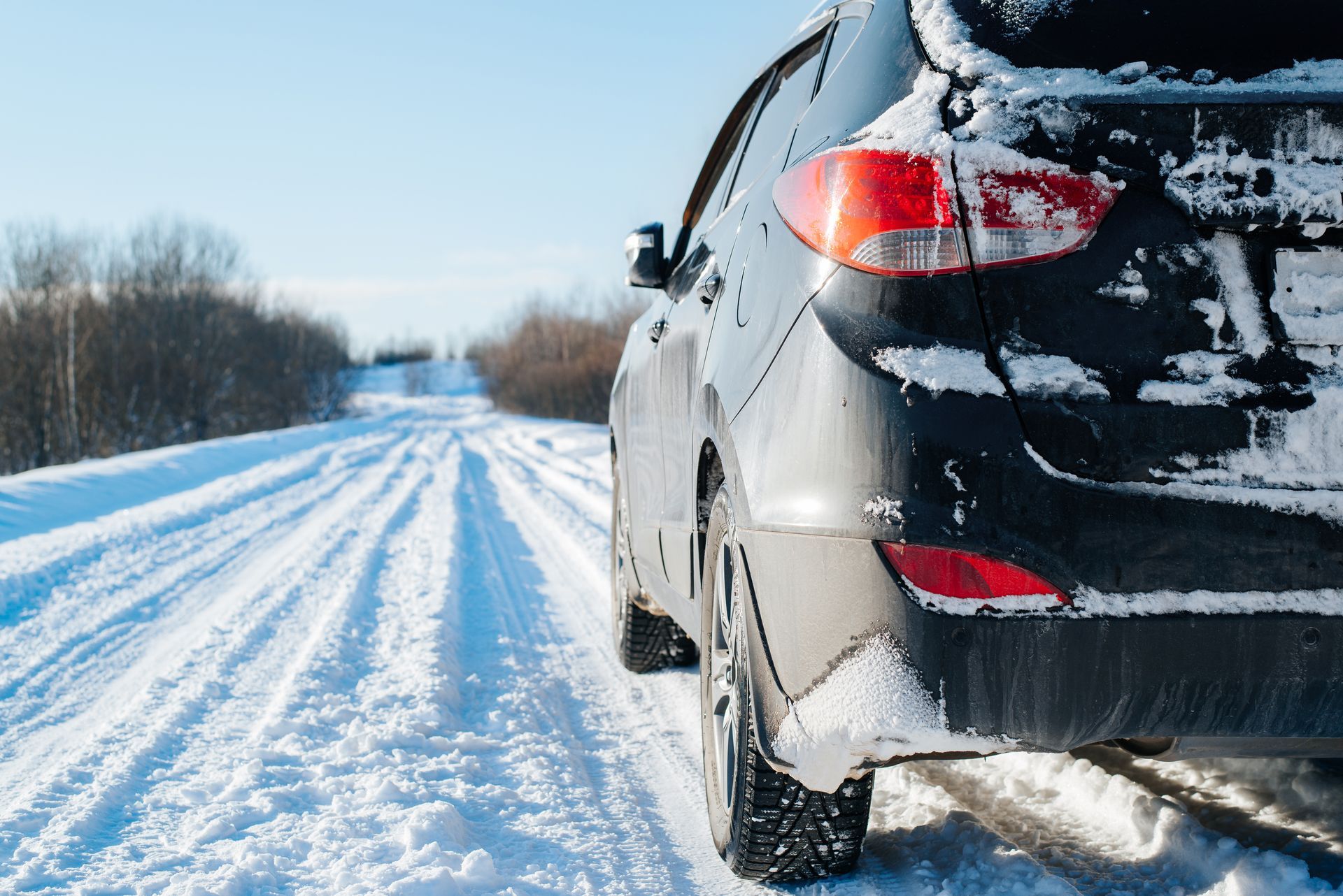 Black SUV driving on a snow-covered road on a sunny day.