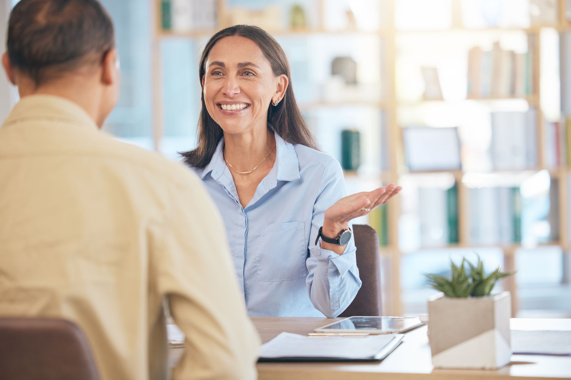 Woman gesturing and smiling at a person across a table in an office setting.