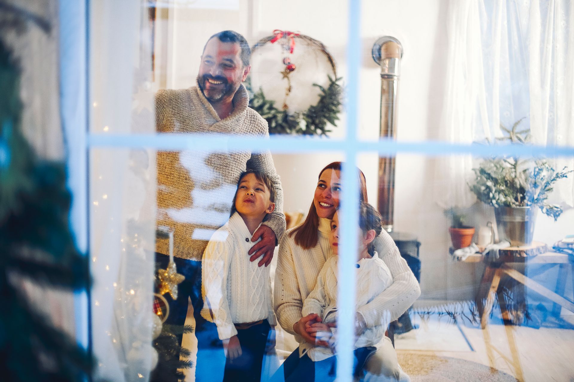 Family smiling, viewed through a window, decorated for Christmas.