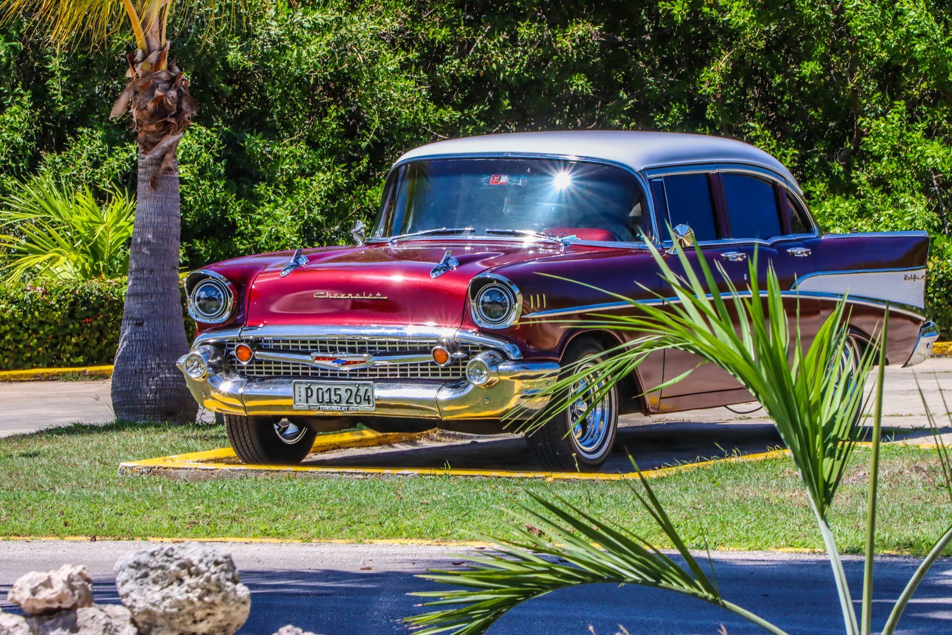 Classic red and silver Chevrolet Bel Air parked in front of tropical foliage.
