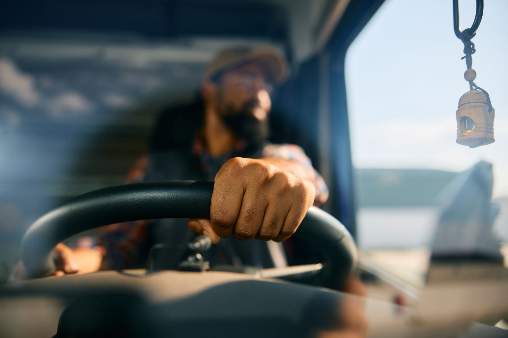 Driver's hand on steering wheel inside truck cab. Blurred figure of driver looking out window.