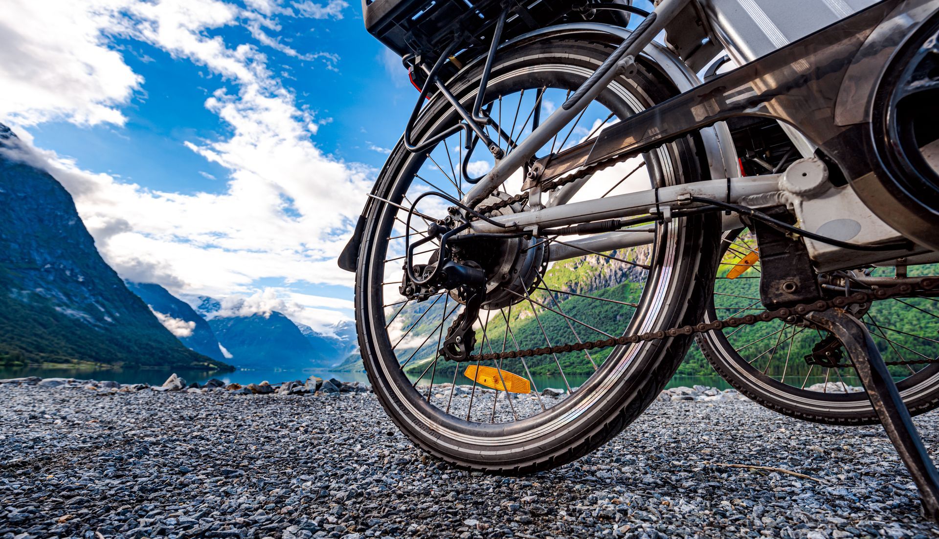 Bicycle wheel and drivetrain against a mountain landscape with blue sky and water.
