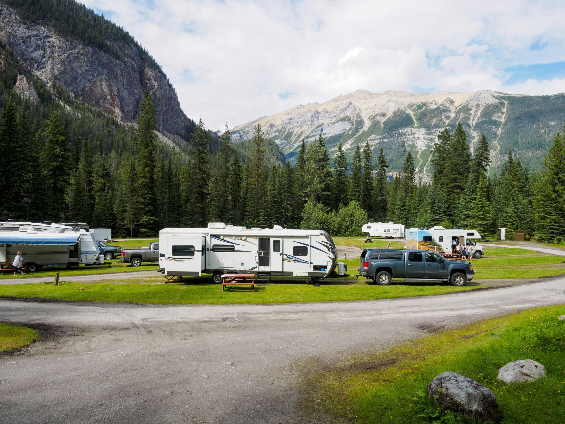 Three people lean out of a camper window, smiling and looking out at the scenery.