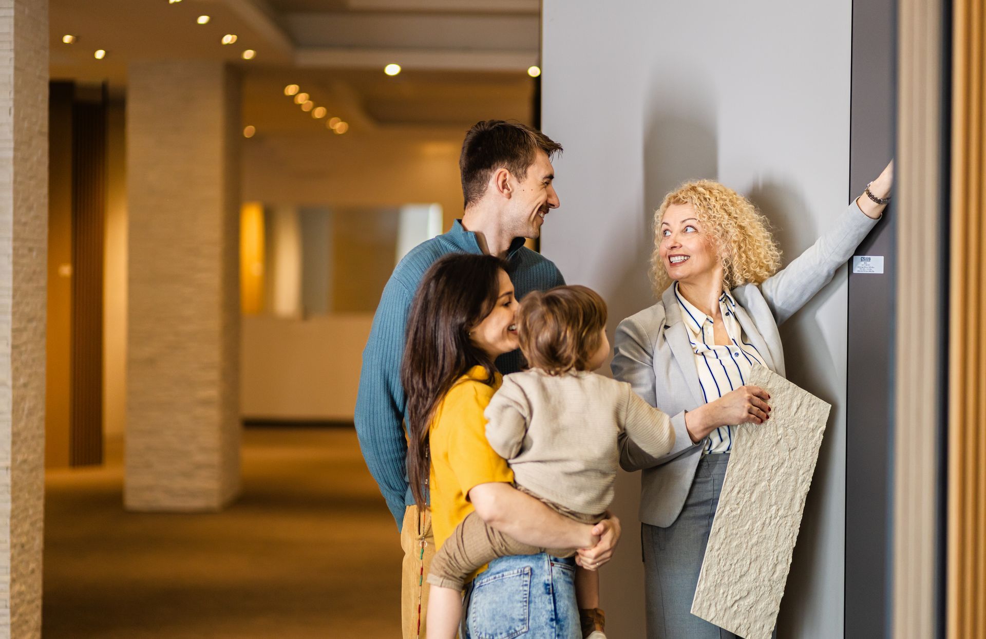 Family with child consults with a blonde designer about textures in a showroom.