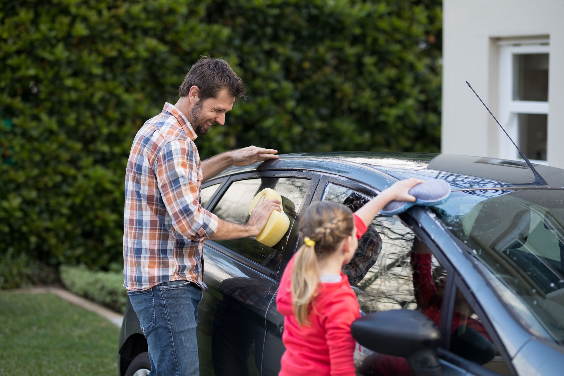 Man and child washing a dark blue car together outdoors.