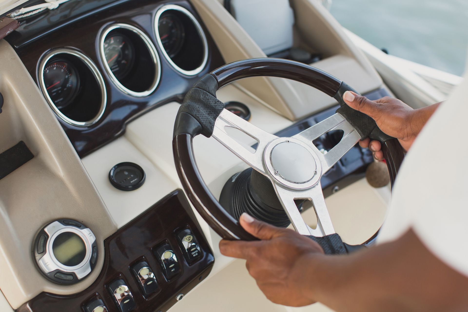 Person's hands gripping a boat steering wheel, controlling the vessel. Dashboard details visible: gauges and cup holders.