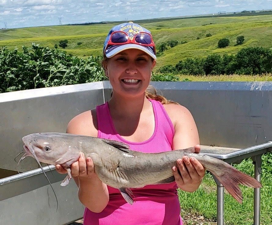 A woman in a pink tank top is holding a large fish