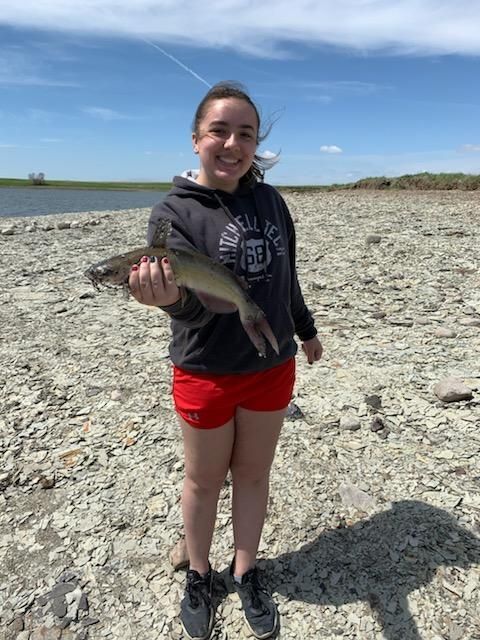 A young girl is holding a fish in her hands on a rocky beach.