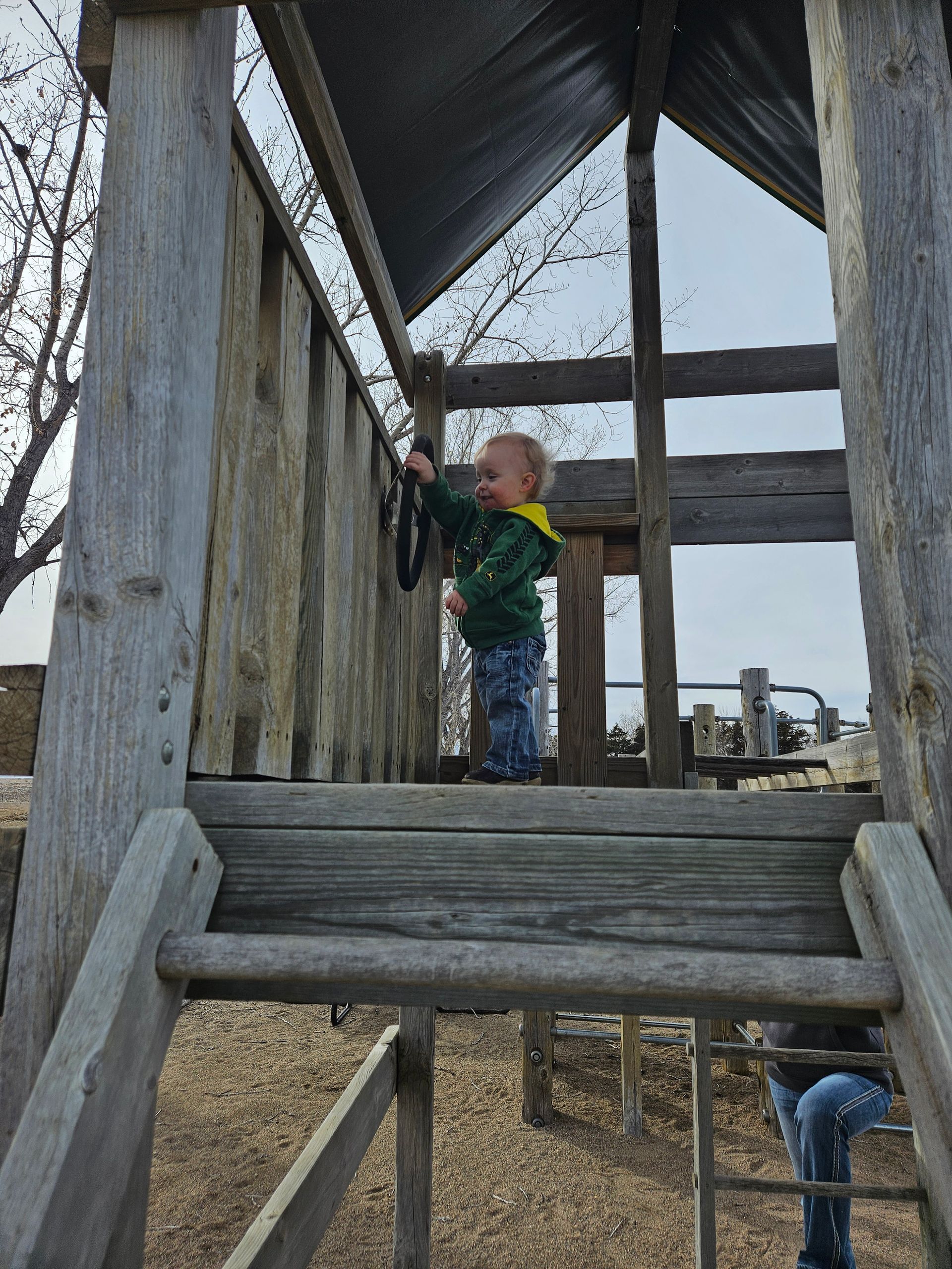 A little boy is standing on top of a wooden playground structure.