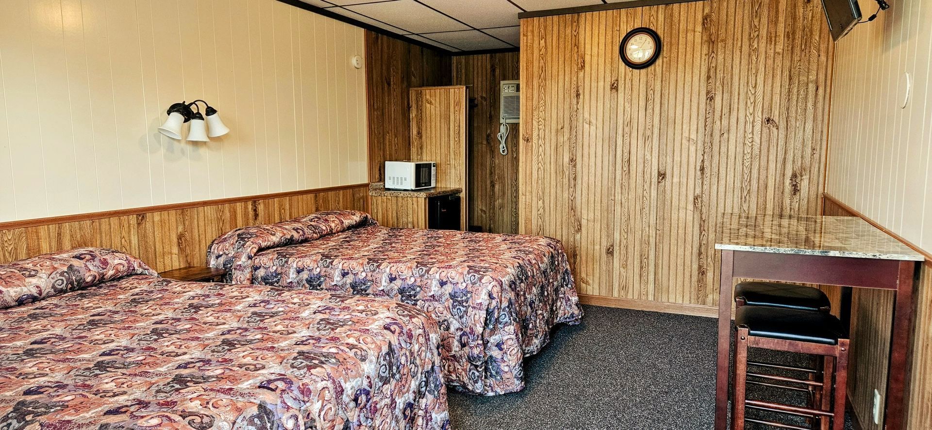 A hotel room with two beds , a table and a clock on the wall.