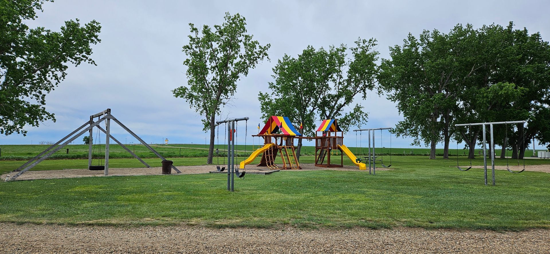 A playground with a slide and swings in a field with trees in the background