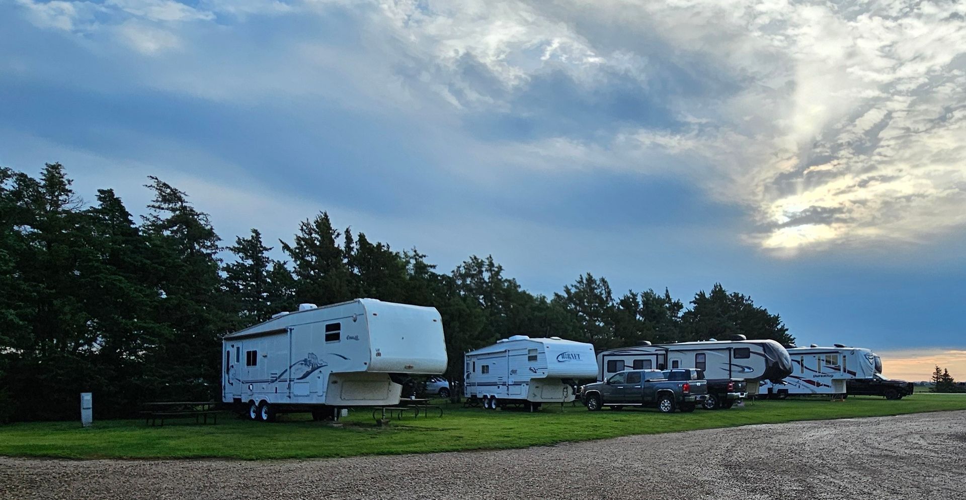 A row of rv 's are parked in a grassy area under a cloudy sky