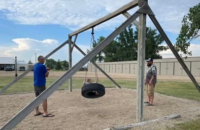 Two men are standing in front of a tire swing.