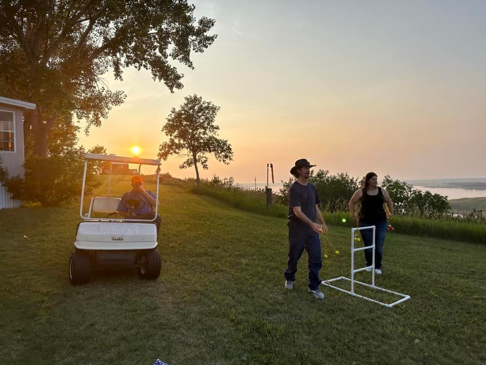 A man and a woman are playing croquet in a yard with a golf cart in the background.