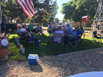 A group of people are sitting in a circle in the grass with an american flag in the background