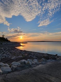 A sunset over a body of water with rocks on the shore.