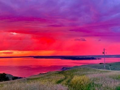A colorful sunset over a body of water with a field in the foreground.