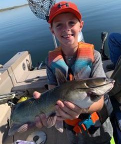 A young boy is holding a catfish on a boat.