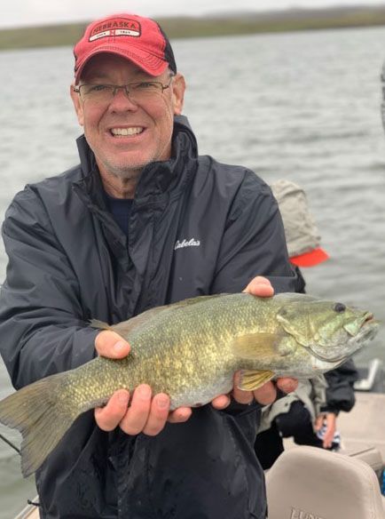 A man in a red hat is holding a large fish in his hands.