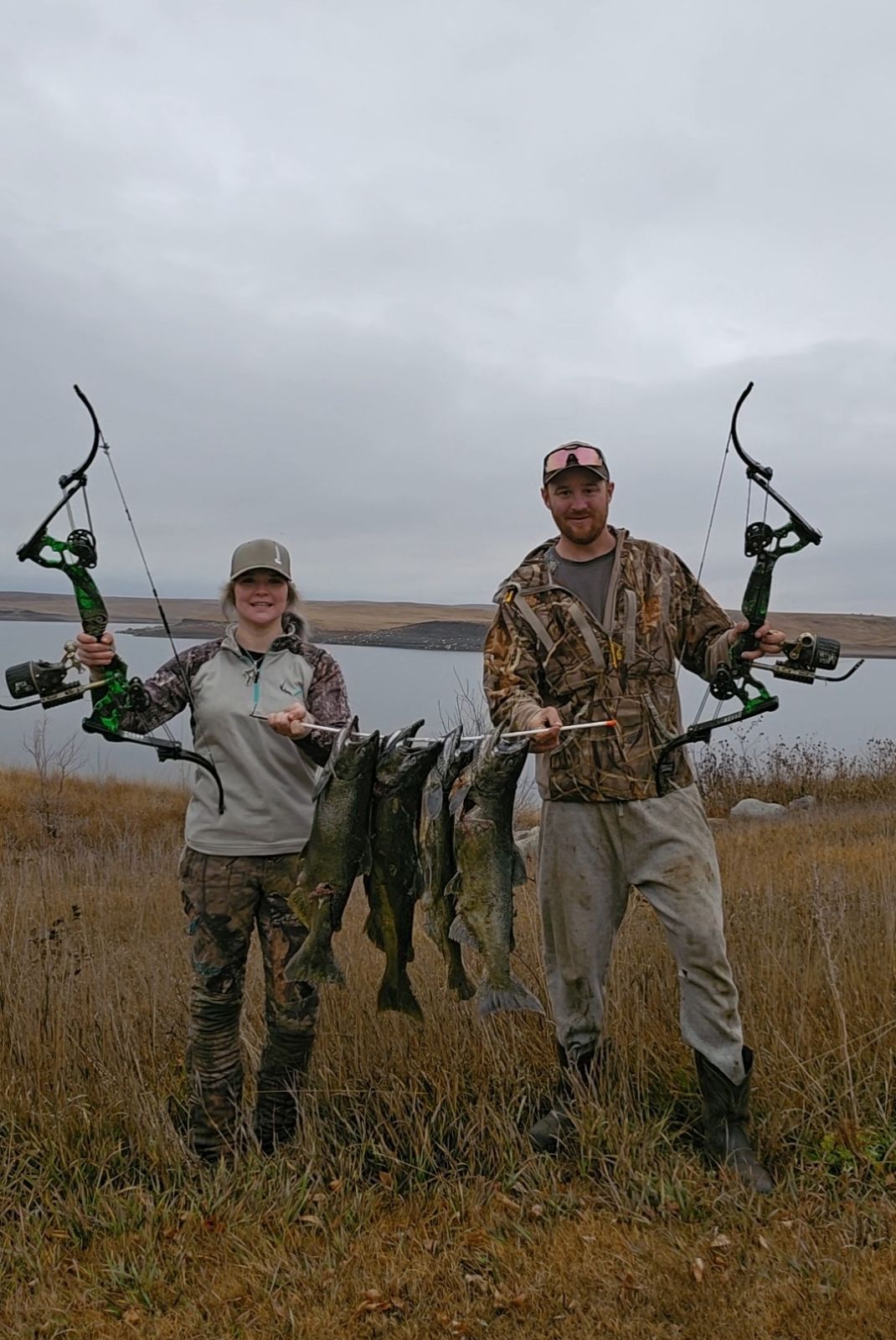 A man and a woman are standing in a field holding bows and arrows.