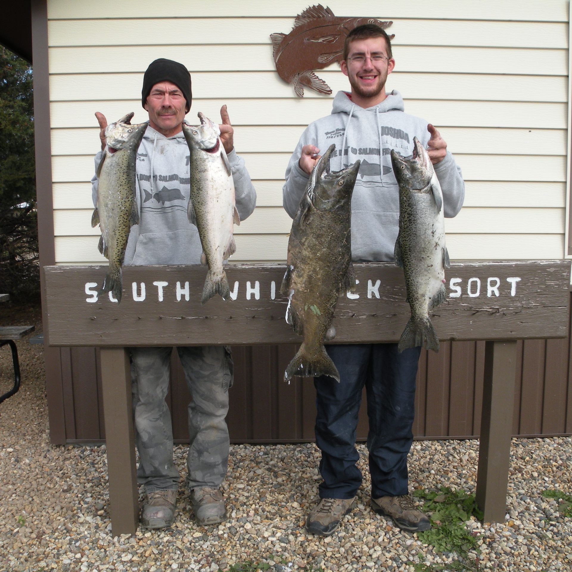 Two men holding fish in front of a sign that says south jhi ck sort