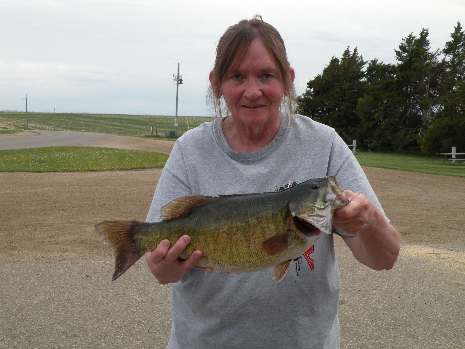 A woman in a grey shirt is holding a large fish