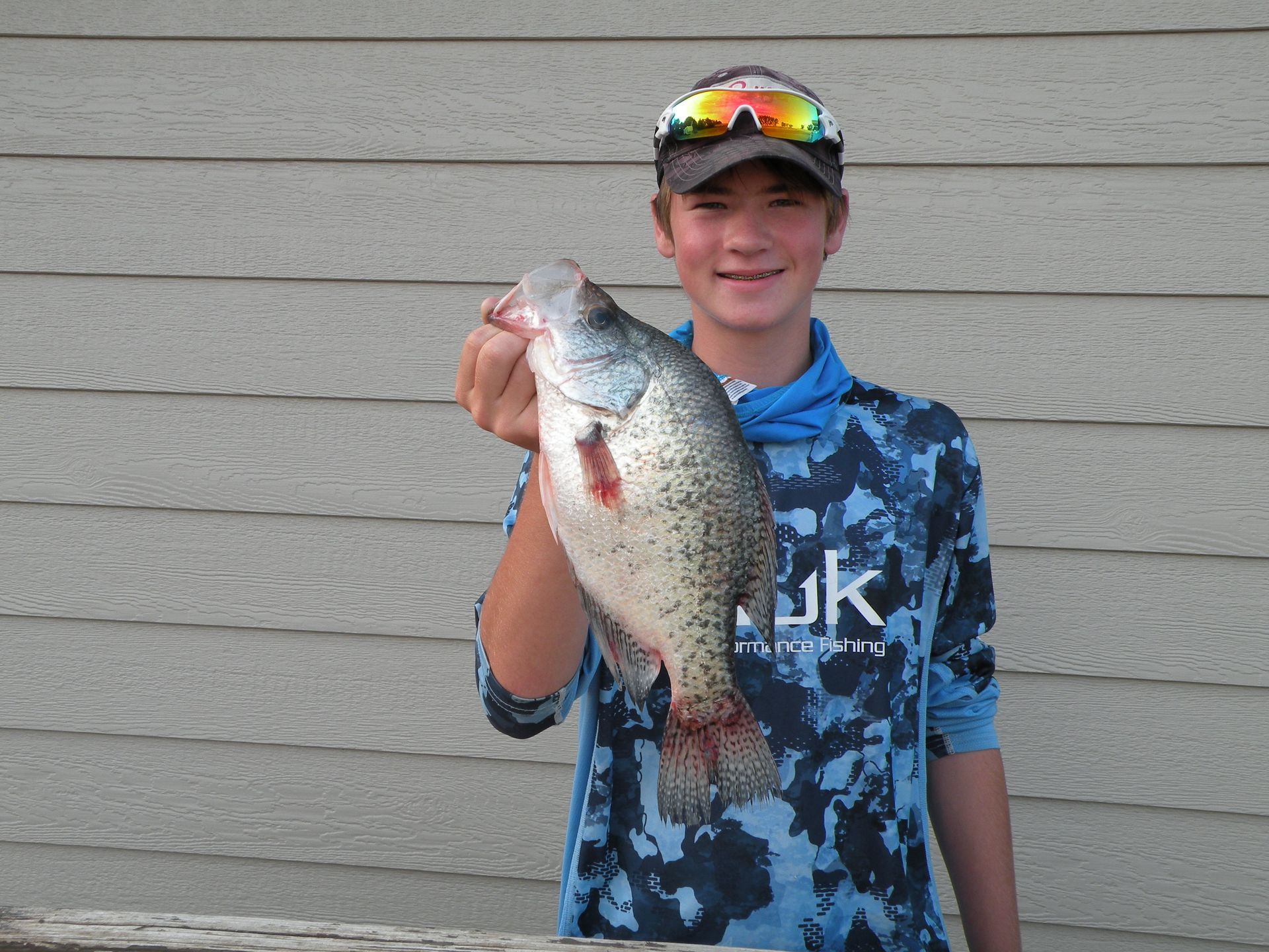 A young boy is holding a large fish in his hand.