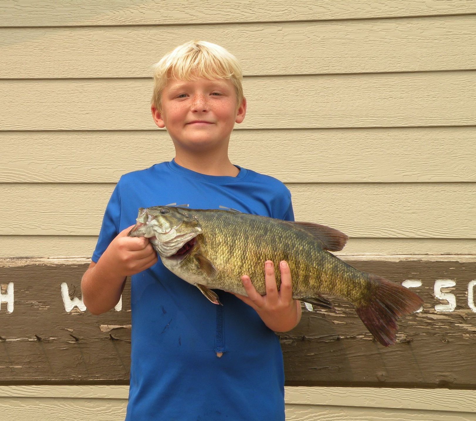 A young boy in a blue shirt is holding a large fish