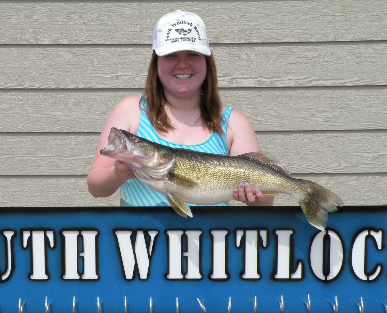 A woman is holding a large fish in front of a sign that says south whitloc