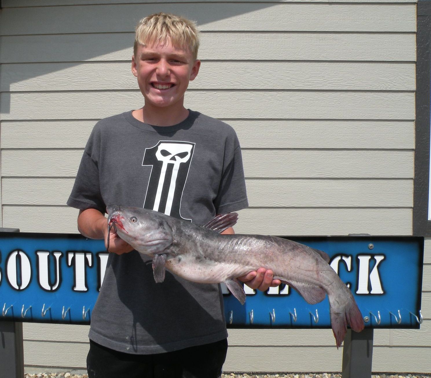 A boy holding a fish in front of a sign that says outback