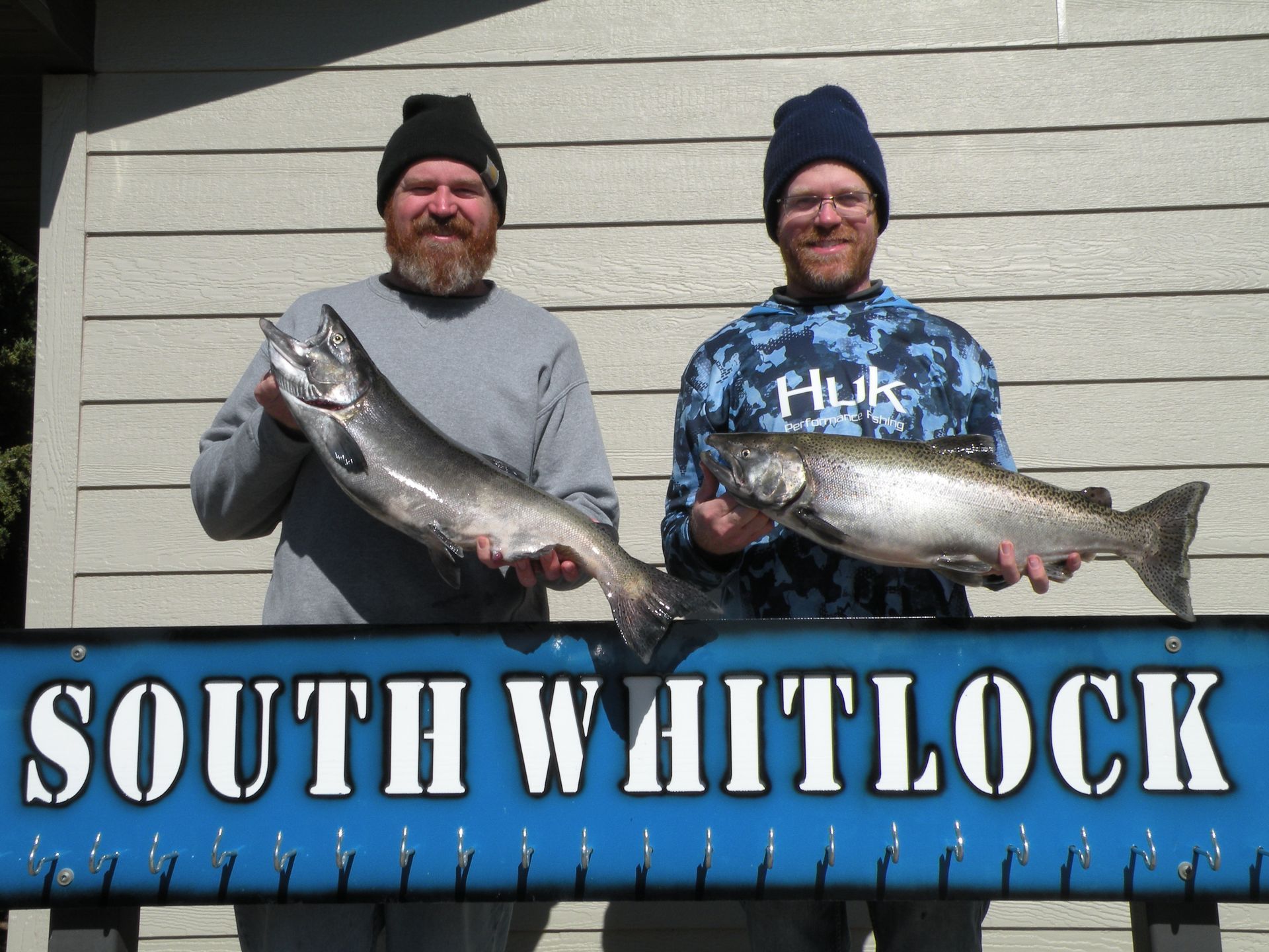 Two men holding fish in front of a sign that says south whitlock