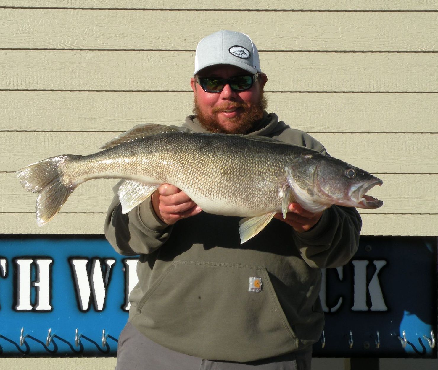 A man holding a large fish in front of a sign that says hw