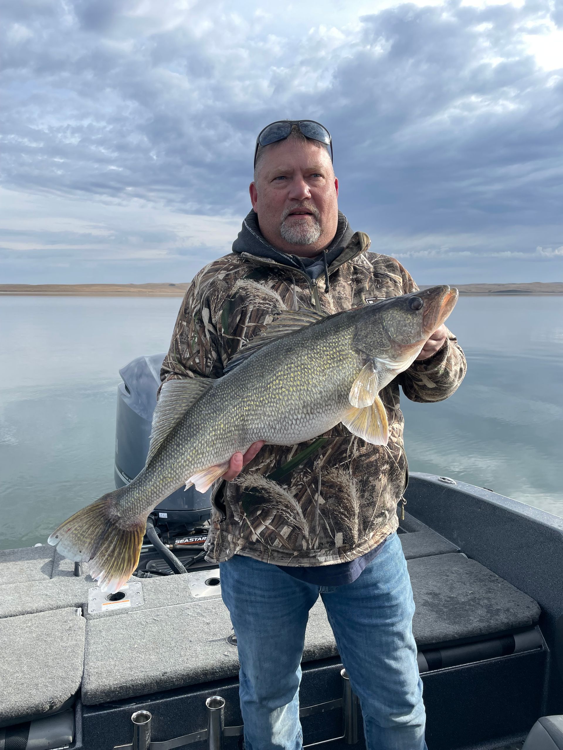 A man is standing on a boat holding a large fish.