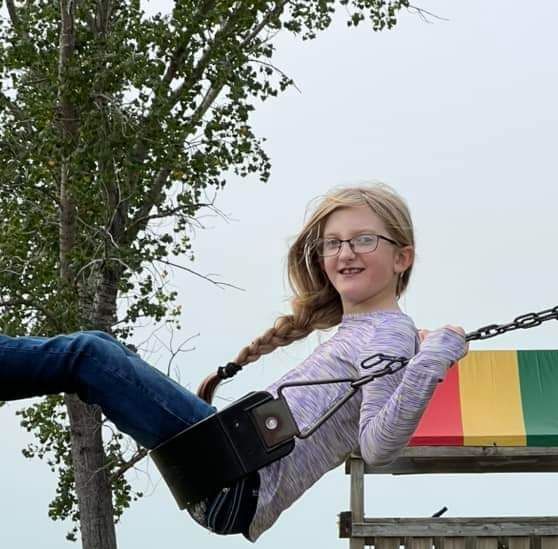 A young girl wearing glasses is sitting on a swing.