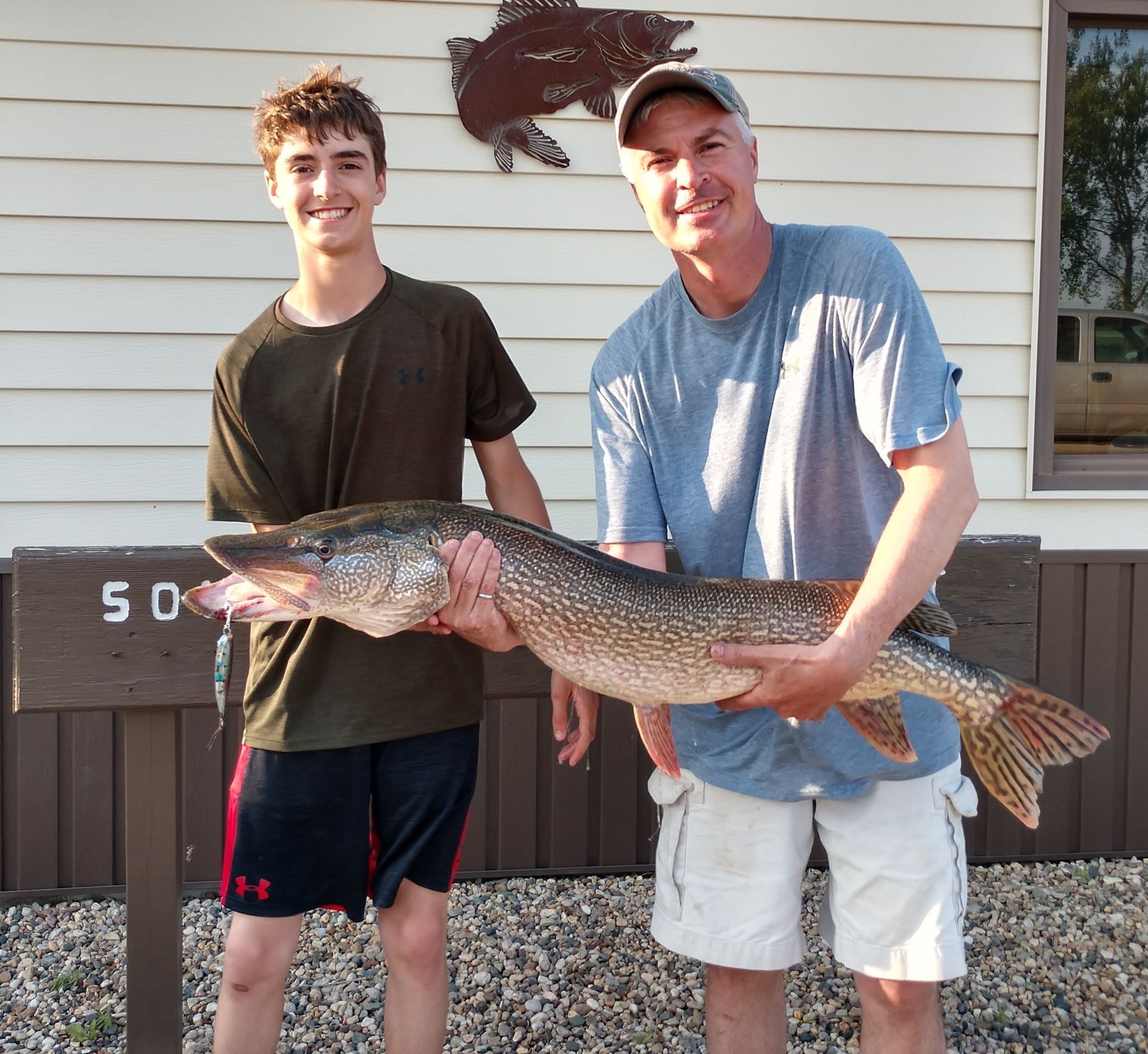 Two men holding a large fish in front of a sign that says 50