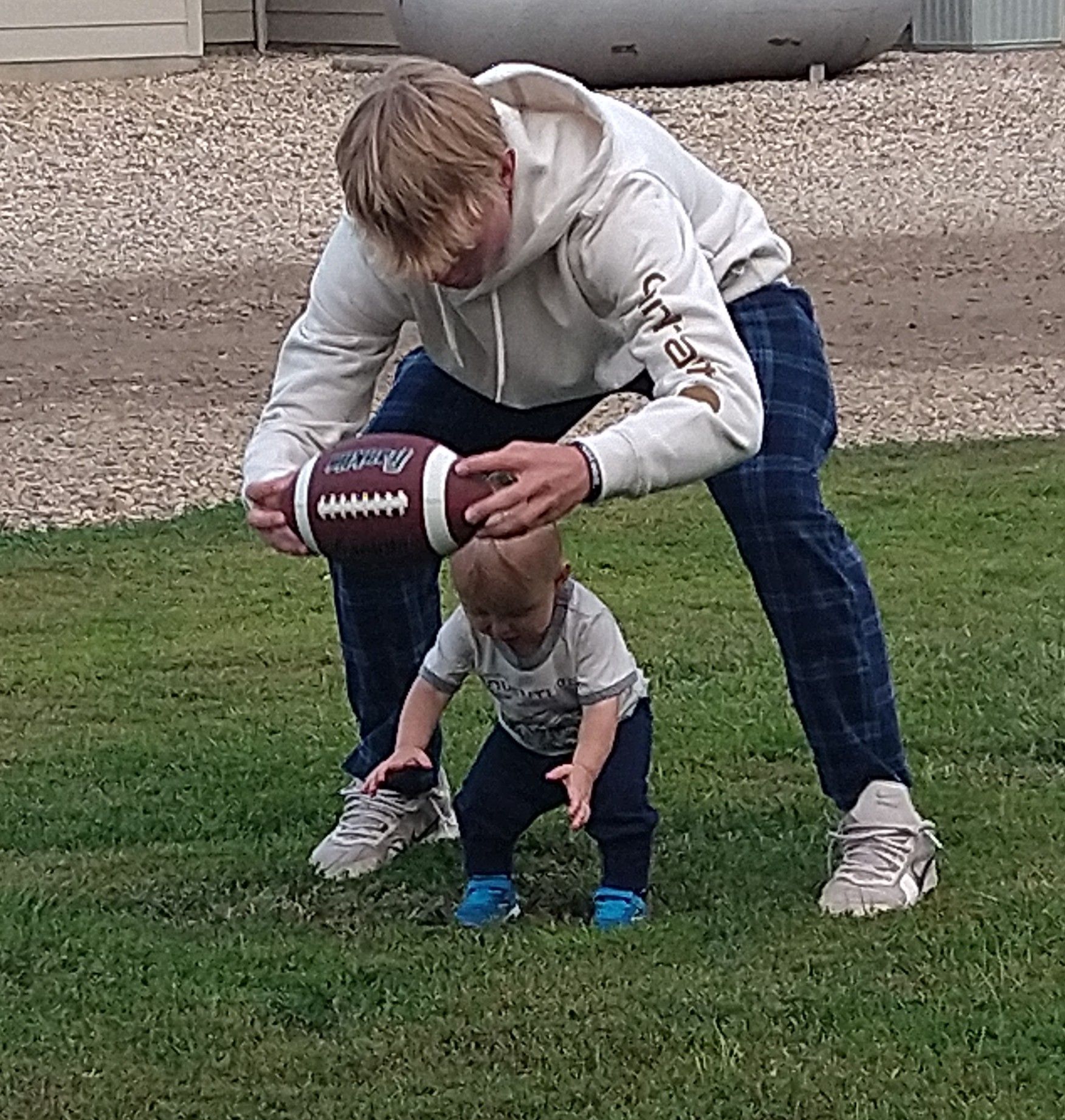 A man and a baby are playing with a football in the grass.