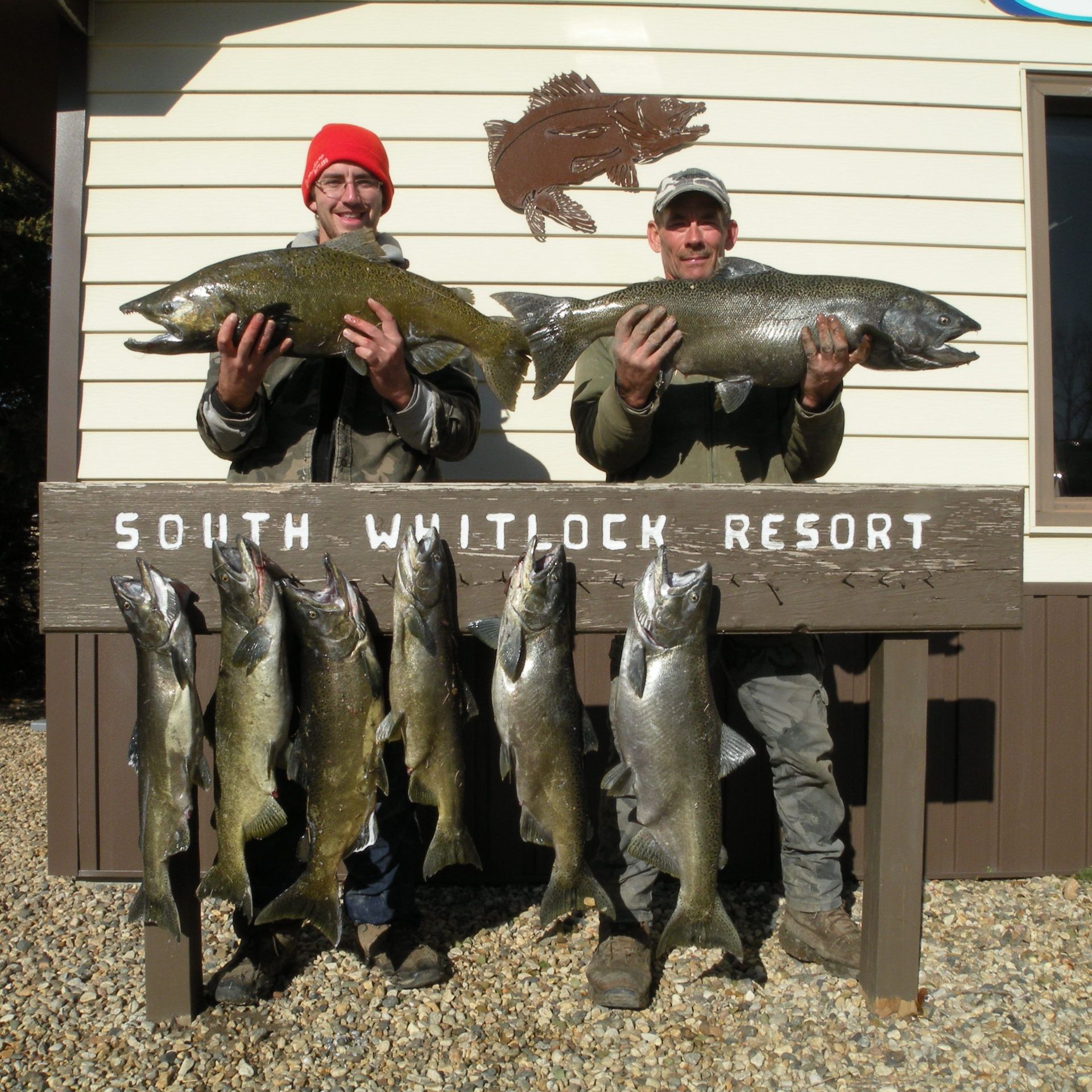 Two men holding large fish in front of a sign that says south whitlock resort