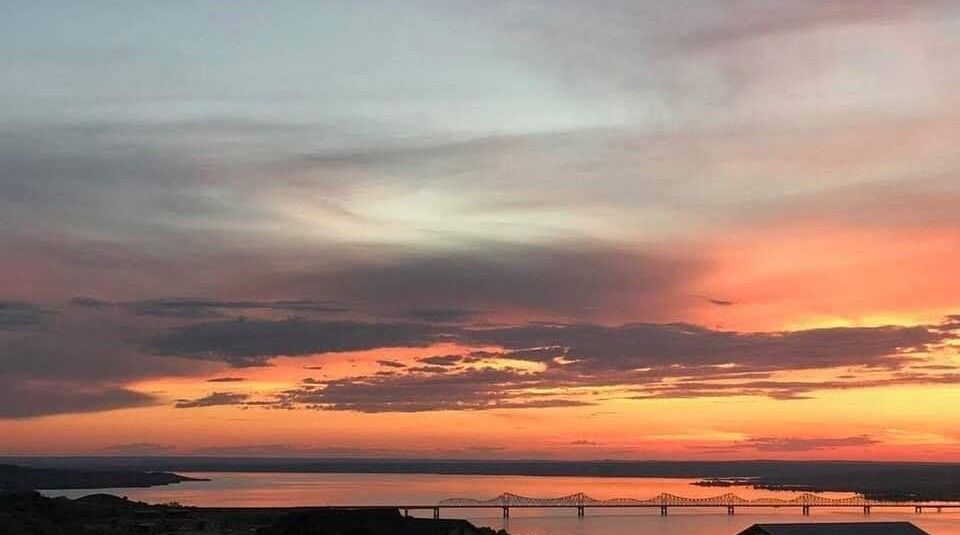 A sunset over a body of water with a bridge in the distance.