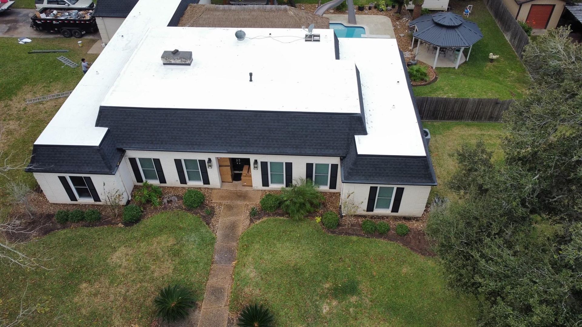An aerial view of a large white house with a black roof.